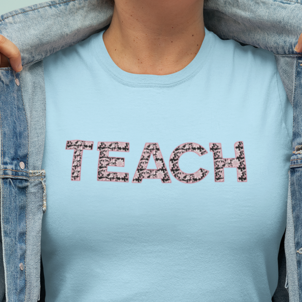 Light blue t-shirt with 'TEACH' printed on it, worn by a person.