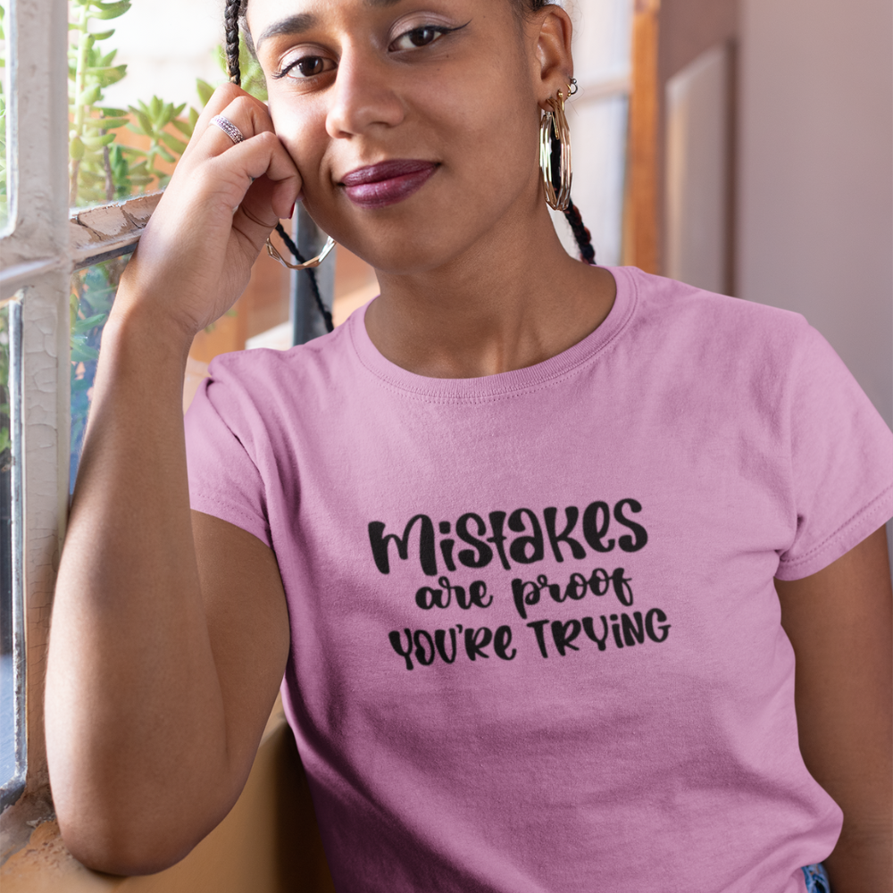 Woman wearing a pink t-shirt with text, standing indoors.
