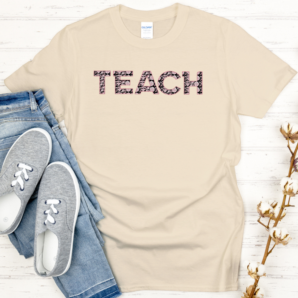 Beige t-shirt with 'TEACH' text, jeans, and sneakers on a white wooden surface.
