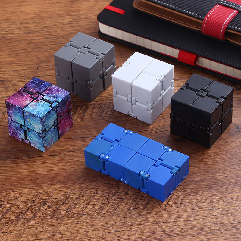 Five different colored fidget cubes on a wooden surface with a notebook in the background.