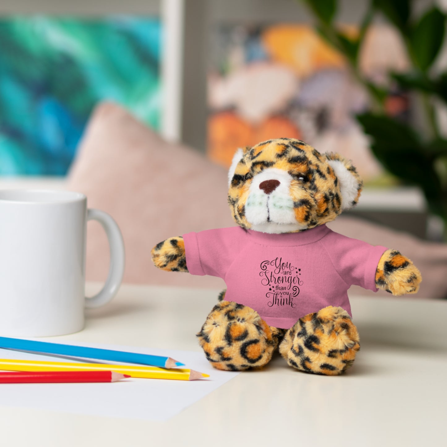 Leopard print teddy bear wearing a pink shirt with text on a desk with stationery items.