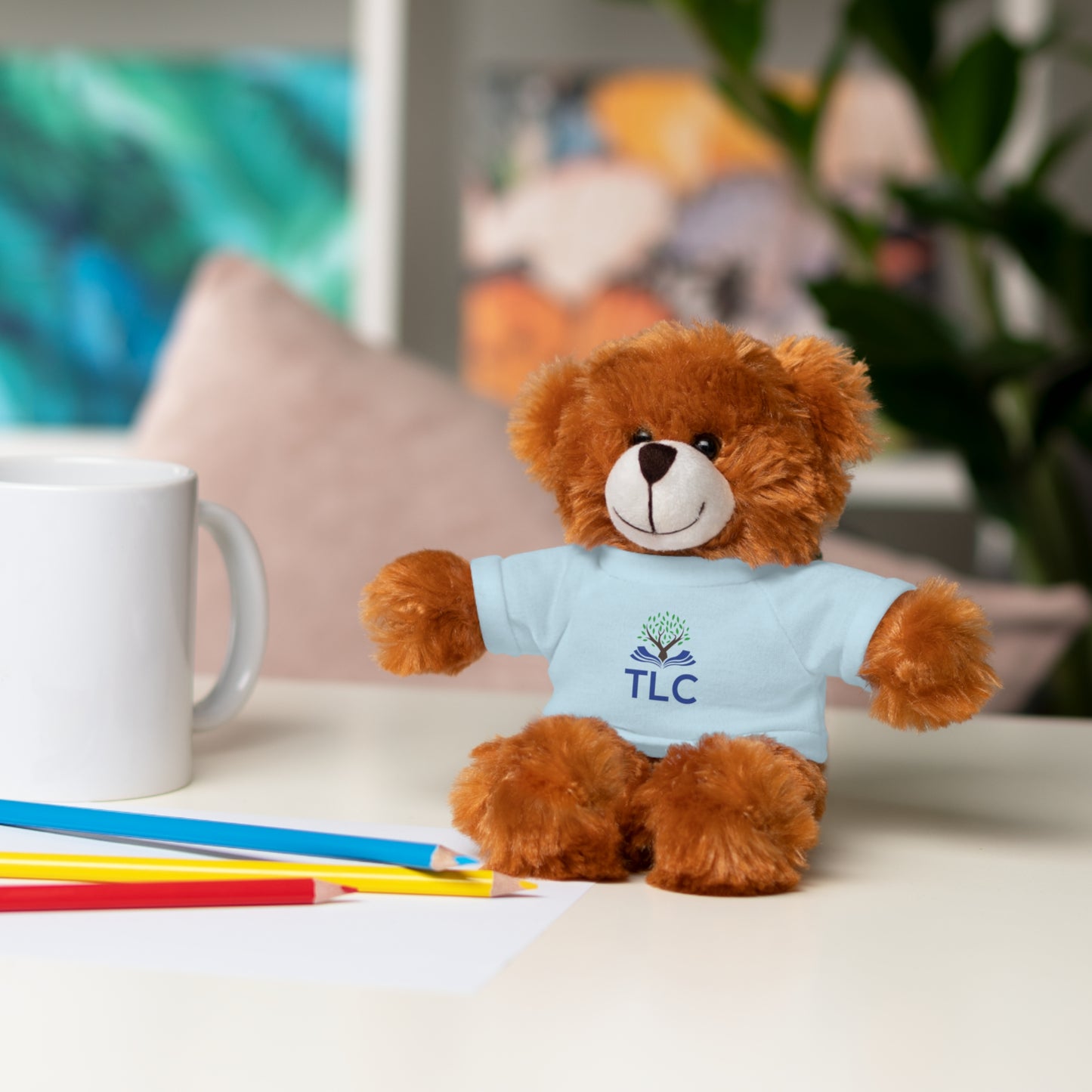 Teddy bear wearing a blue shirt with 'TLC' on a table with stationery items.