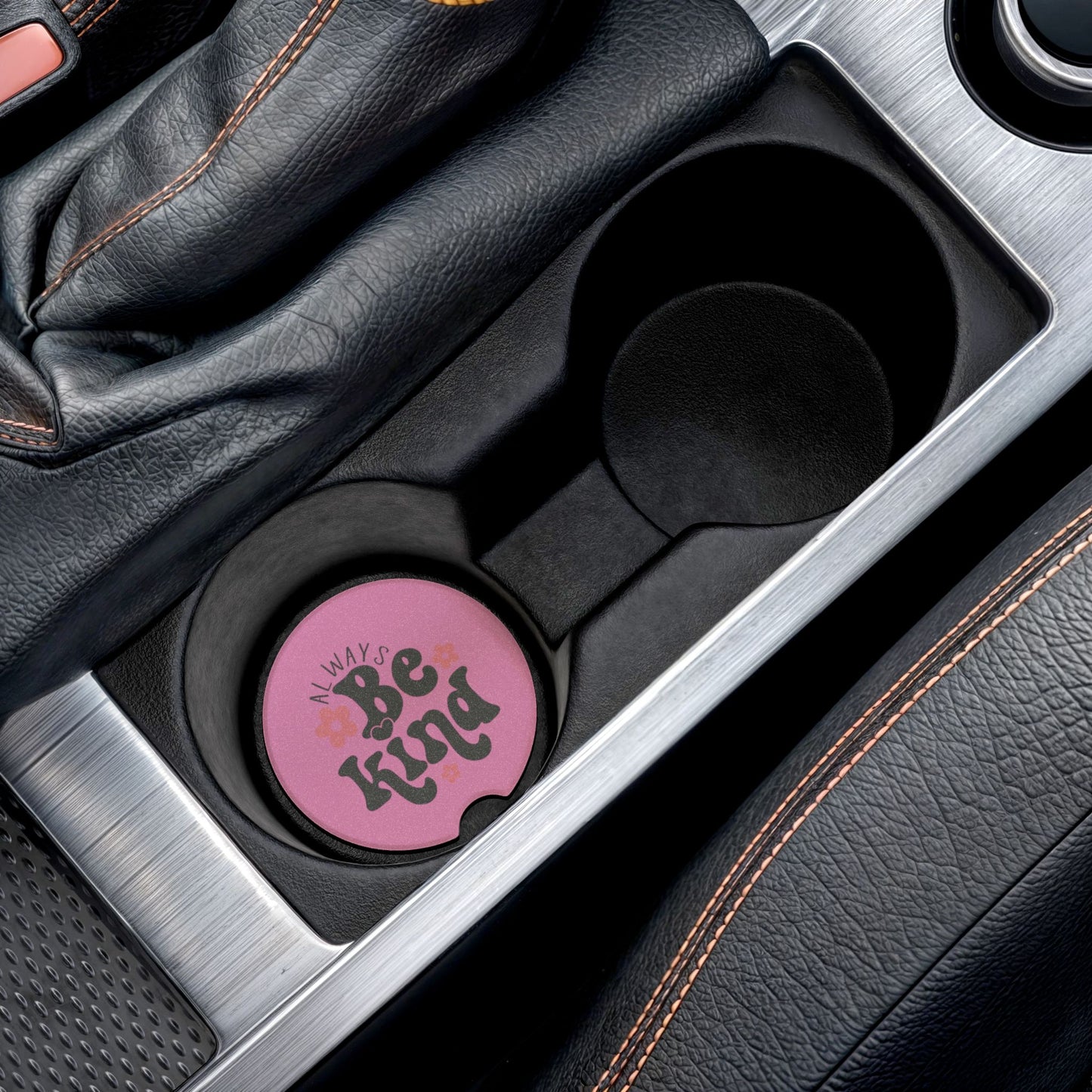 Pink car cup holder cover with 'Always Be Kind' text in a car's center console.