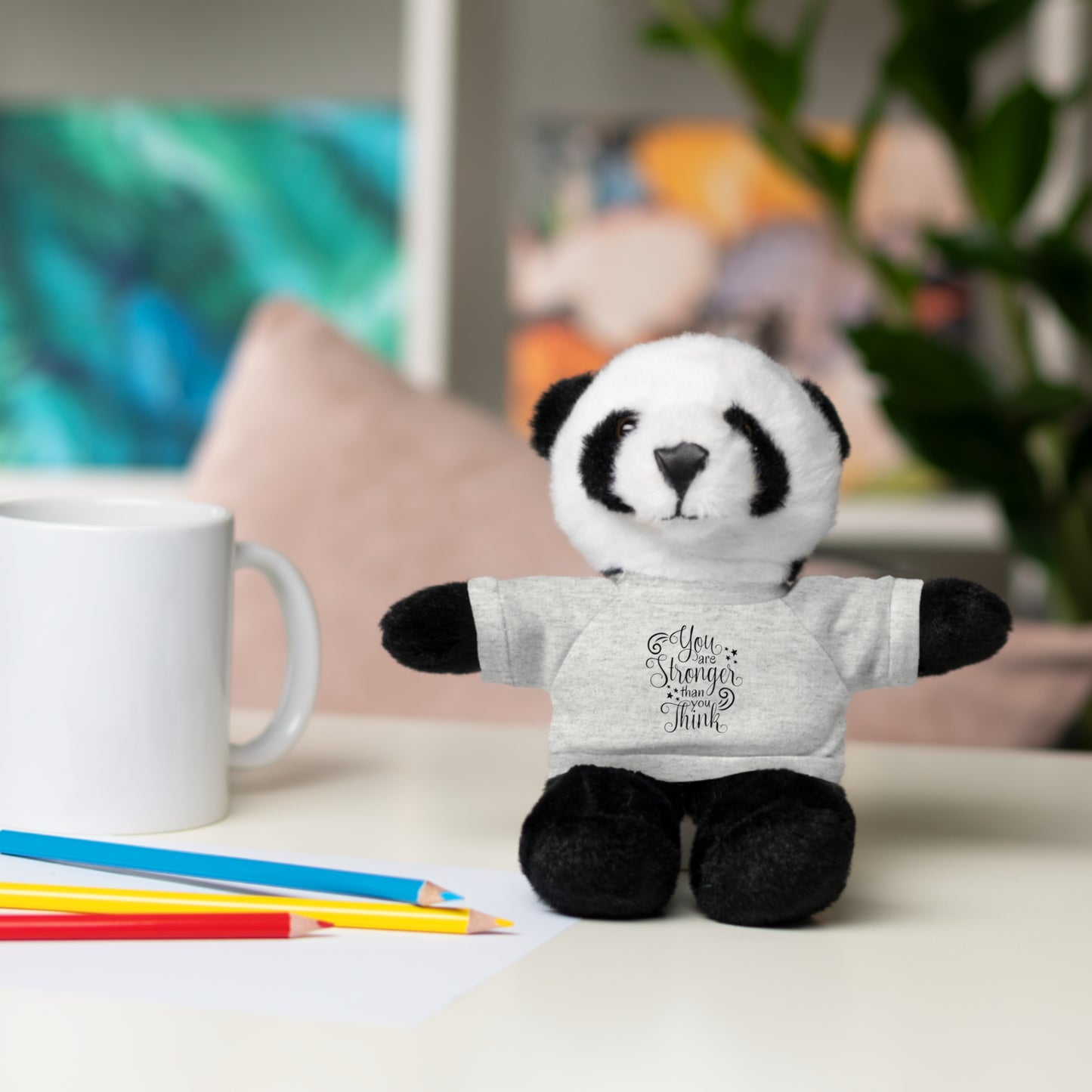 Plush panda toy wearing a t-shirt with text, placed on a table with stationery items.