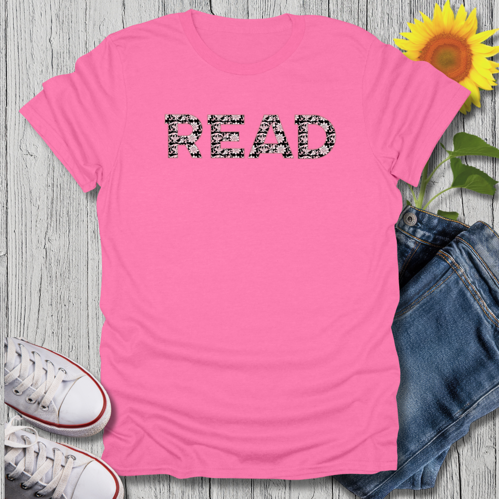 Pink t-shirt with '#READ' text, sunflower, jeans, and sneakers on a wooden surface