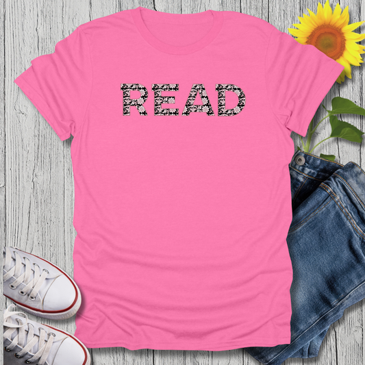 Pink t-shirt with '#READ' text, sunflower, jeans, and sneakers on a wooden surface