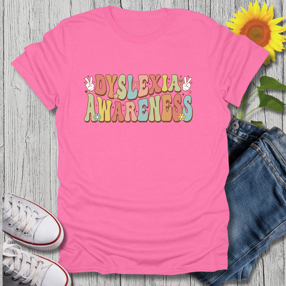 Pink t-shirt with 'Dyslexia Awareness' text on a wooden surface with jeans, sneakers, and a sunflower.