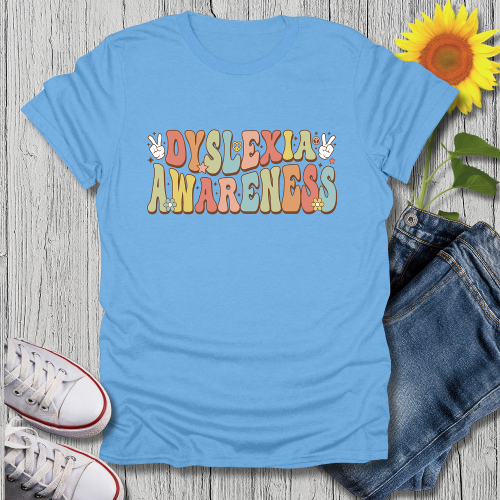 Blue t-shirt with 'Dyslexia Awareness' text on a wooden surface with jeans and sneakers.