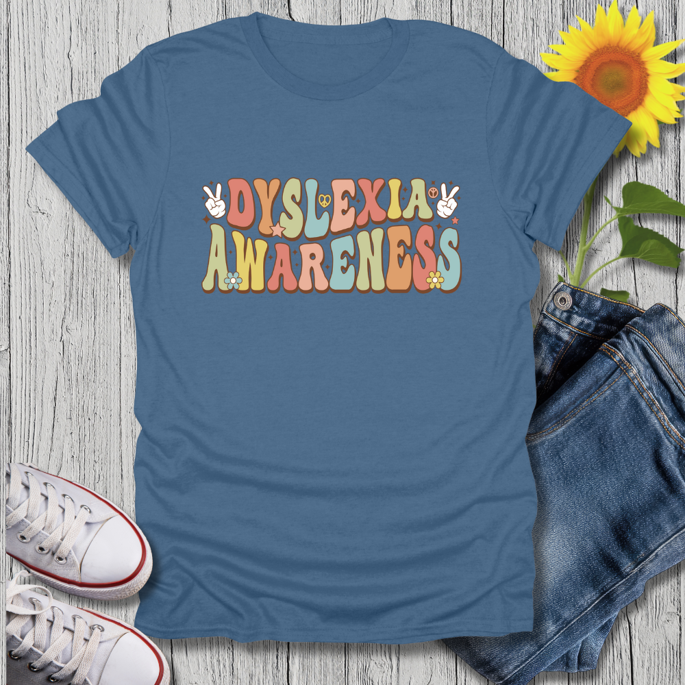 Blue t-shirt with 'Dyslexia Awareness' text on a wooden surface with jeans and sneakers.