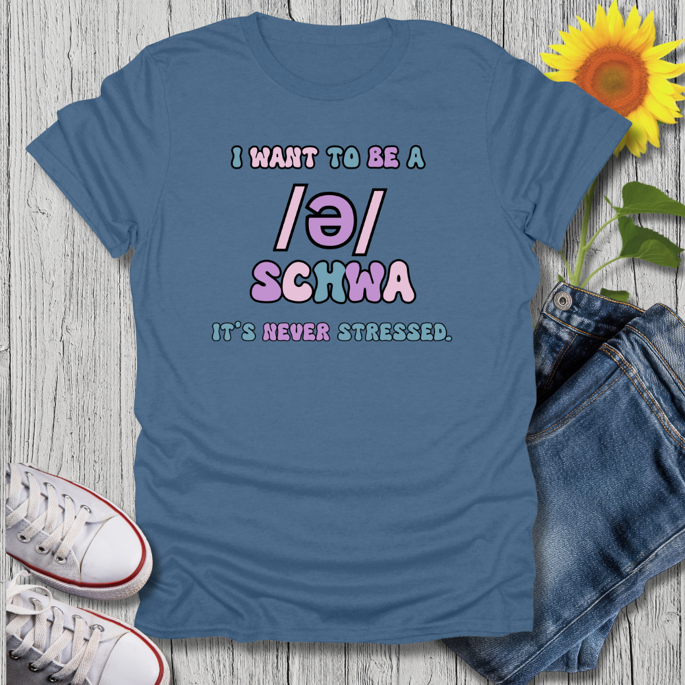 Blue t-shirt with text 'I want to be a /ə/ schwa it's never stressed' on a wooden surface with sneakers and jeans.