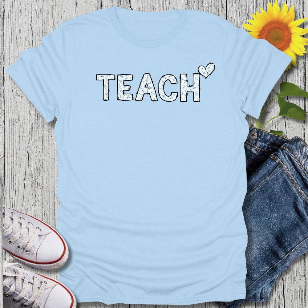 Light blue t-shirt with 'TEACH' text, sunflower, jeans, and sneakers on a wooden surface