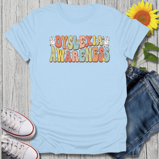 Light blue t-shirt with 'Dyslexia Awareness' text on a wooden surface with jeans and sneakers.