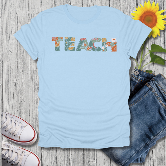 Light blue t-shirt with 'TEACH' printed on it, paired with jeans and sneakers on a wooden surface.