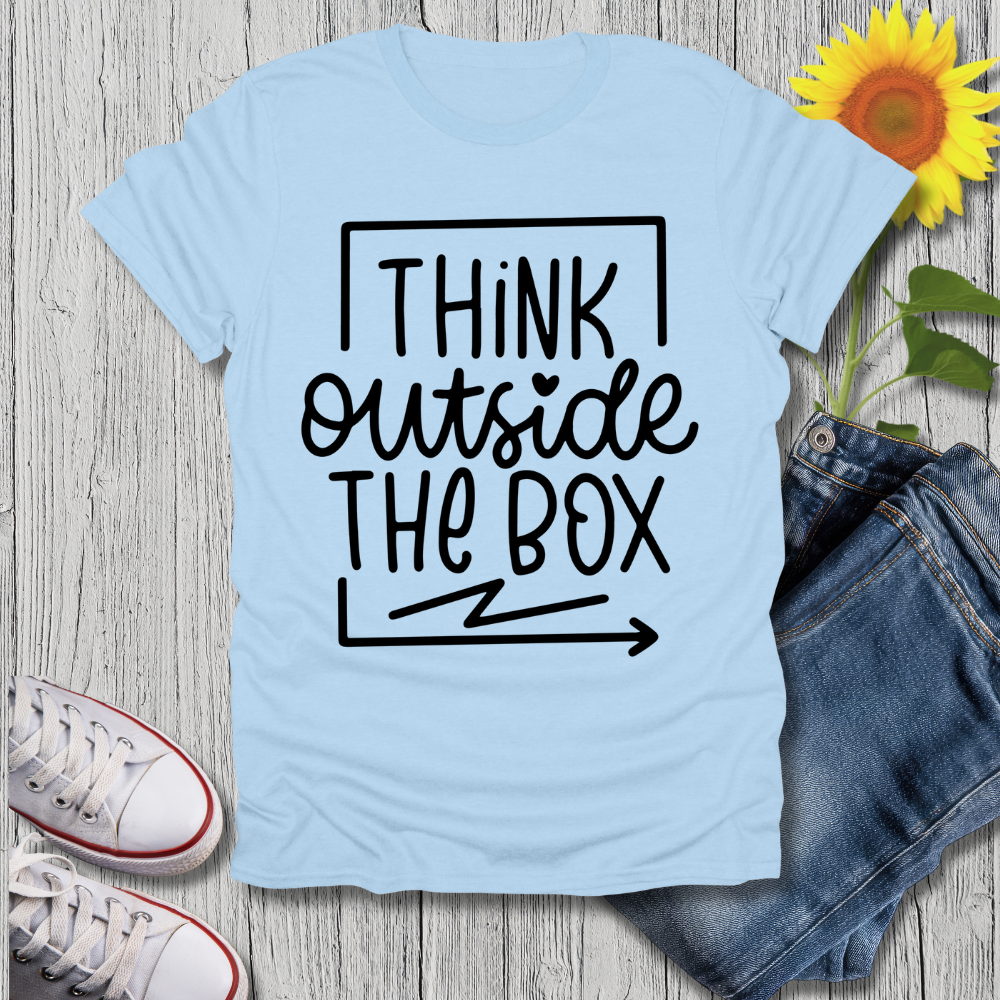 Light blue t-shirt with 'Think Outside The Box' text on a wooden surface with jeans and sneakers.