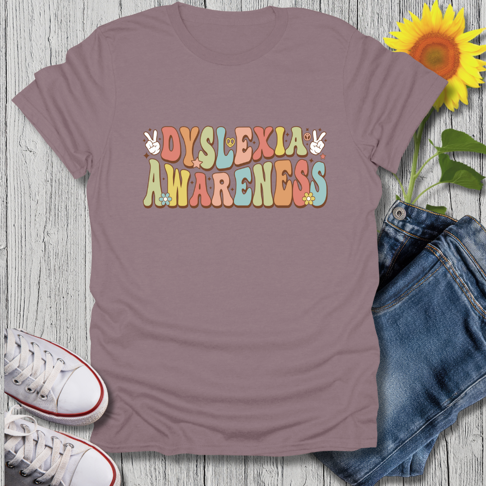 Purple t-shirt with 'Dyslexia Awareness' text on a wooden surface with jeans and sneakers.