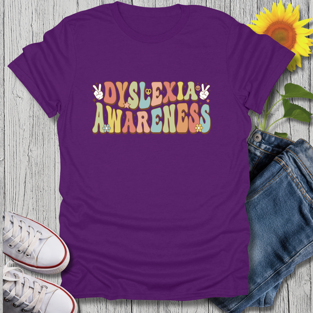 Purple t-shirt with 'Dyslexia Awareness' text on a wooden surface with jeans and sneakers.