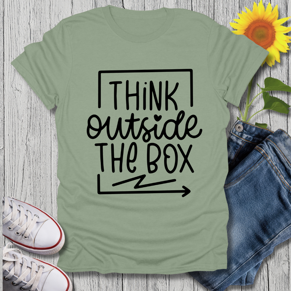 Green t-shirt with 'Think Outside The Box' text on a wooden surface with jeans and sneakers.