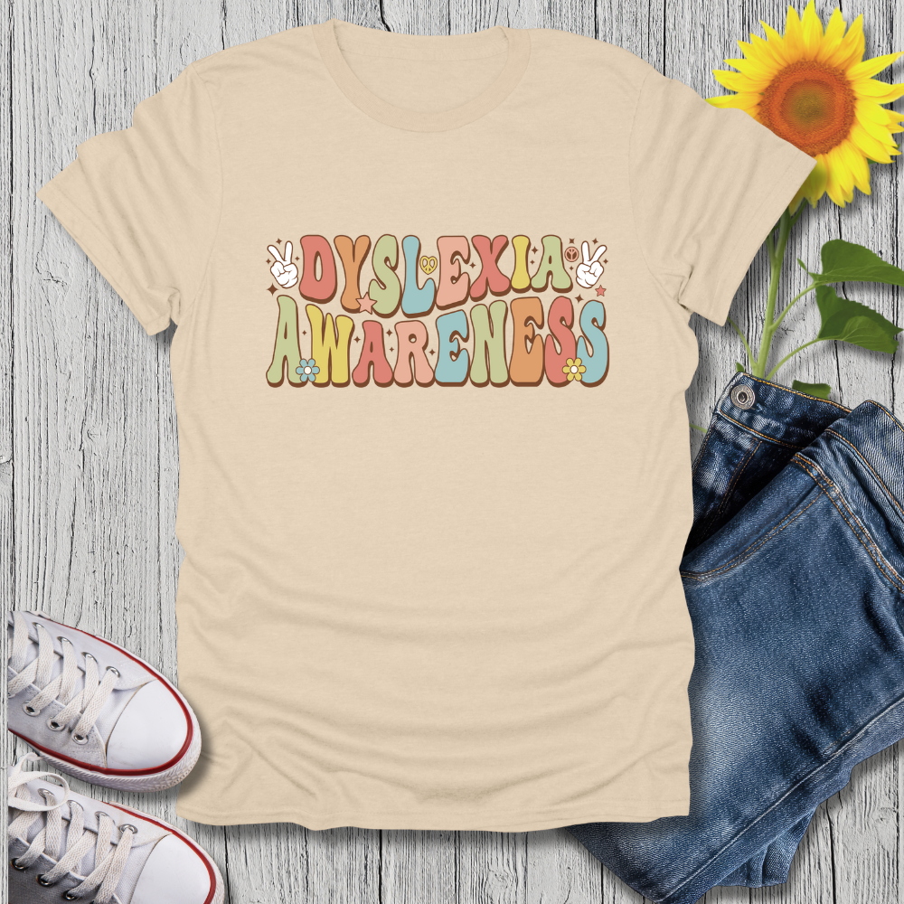 Beige t-shirt with 'Dyslexia Awareness' text, sunflower, jeans, and sneakers on a wooden surface