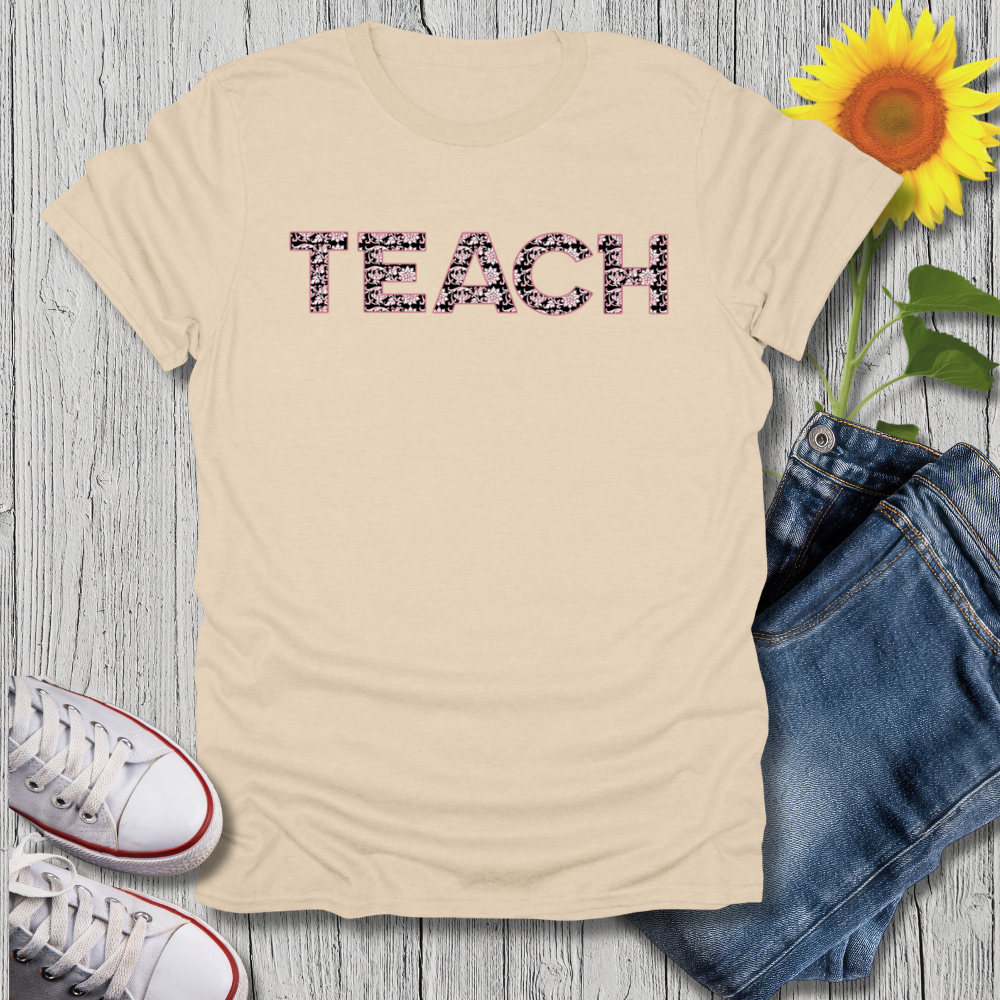 Beige t-shirt with 'TEACH' text, sunflower, jeans, and sneakers on a wooden surface