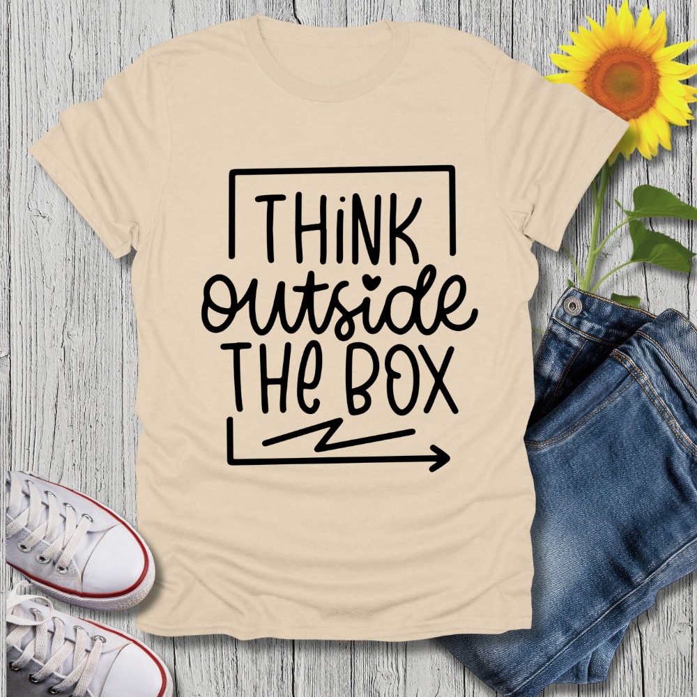 Beige t-shirt with 'Think outside the box' text, white sneakers, blue jeans, and a sunflower on a wooden surface.