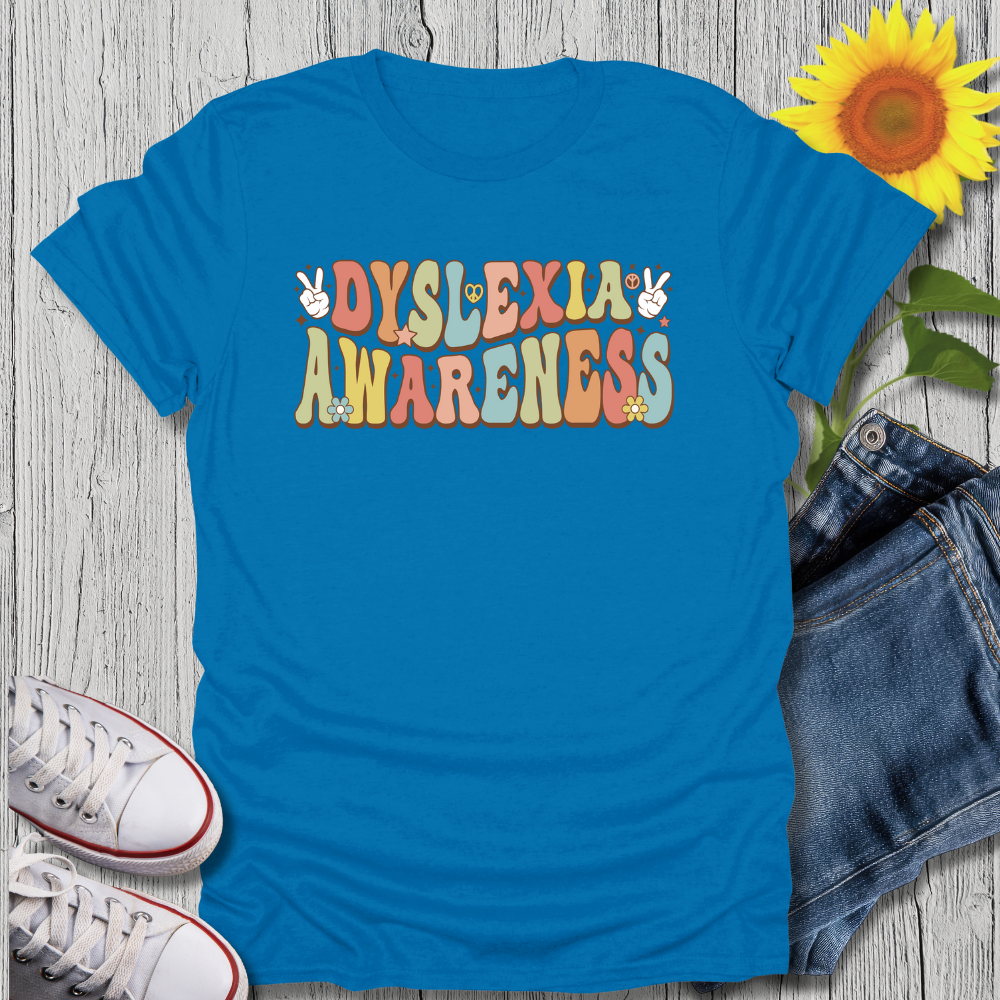 Blue t-shirt with 'Dyslexia Awareness' text on a wooden surface with jeans and sneakers.