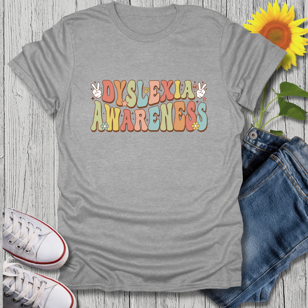Gray t-shirt with 'Dyslexia Awareness' text, sunflower, jeans, and sneakers on a wooden surface