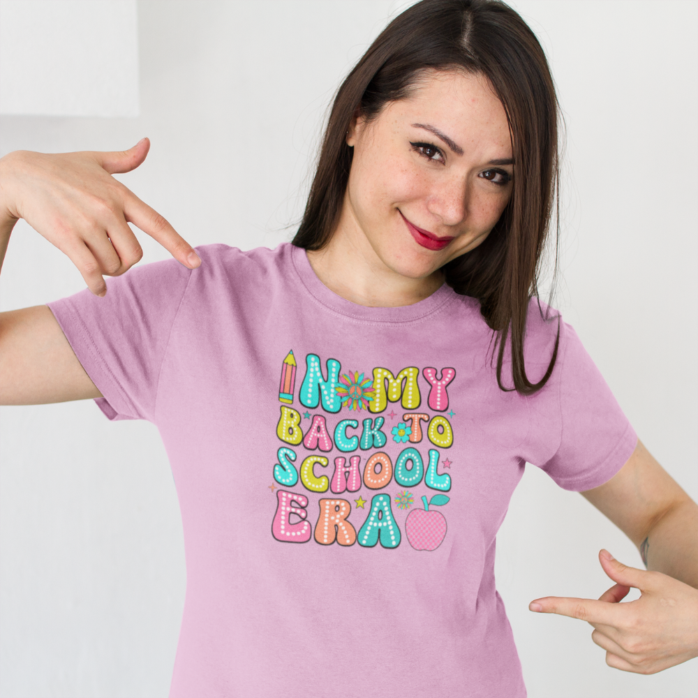 Woman wearing a pink t-shirt with colorful text and pointing to it.