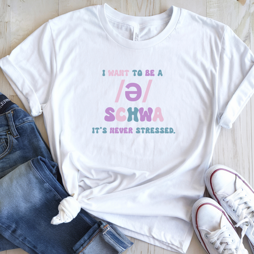 White t-shirt with colorful text on a wooden surface with jeans and sneakers.