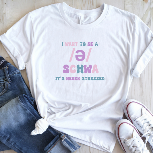 White t-shirt with colorful text on a wooden surface with jeans and sneakers.