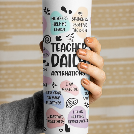 Person holding a book titled 'Teacher Daily Affirmations' with colorful text and graphics on a wooden surface.