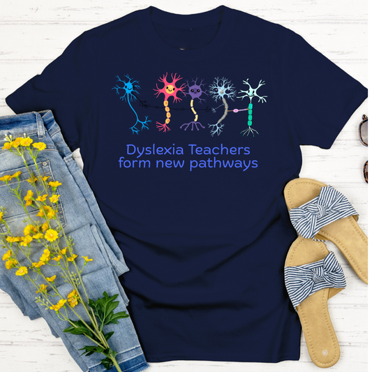 Navy blue t-shirt with colorful neuron graphics and text 'Dyslexia Teachers form new pathways' on a white wooden surface with denim shorts and sandals.