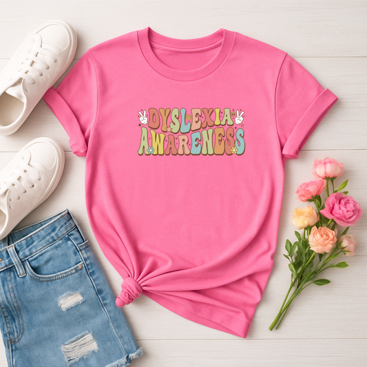 Pink t-shirt with 'Dyslexia Awareness' text on a white surface with jeans, shoes, and flowers.