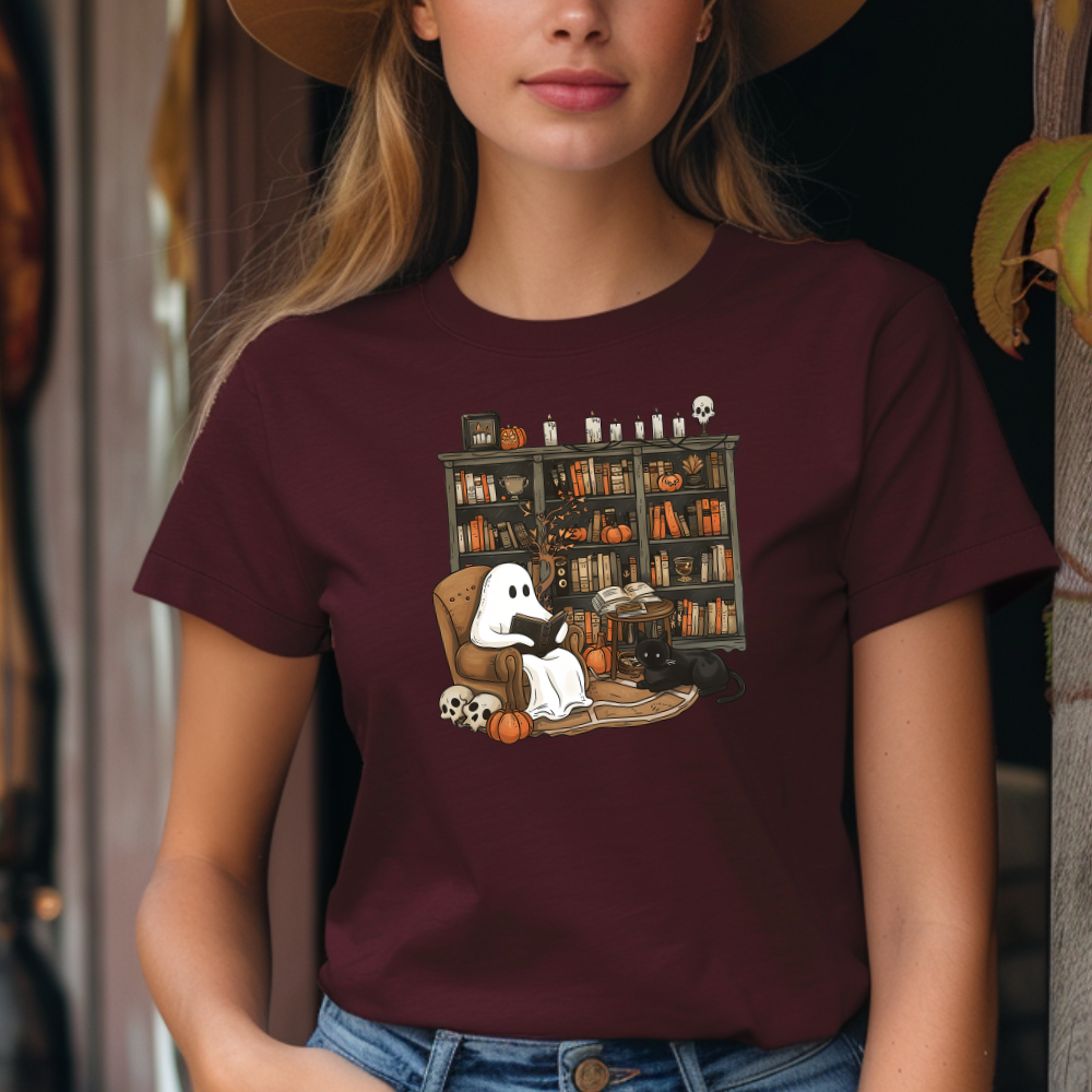 Person wearing a maroon t-shirt with a graphic design of a ghost reading a book in front of a bookshelf.