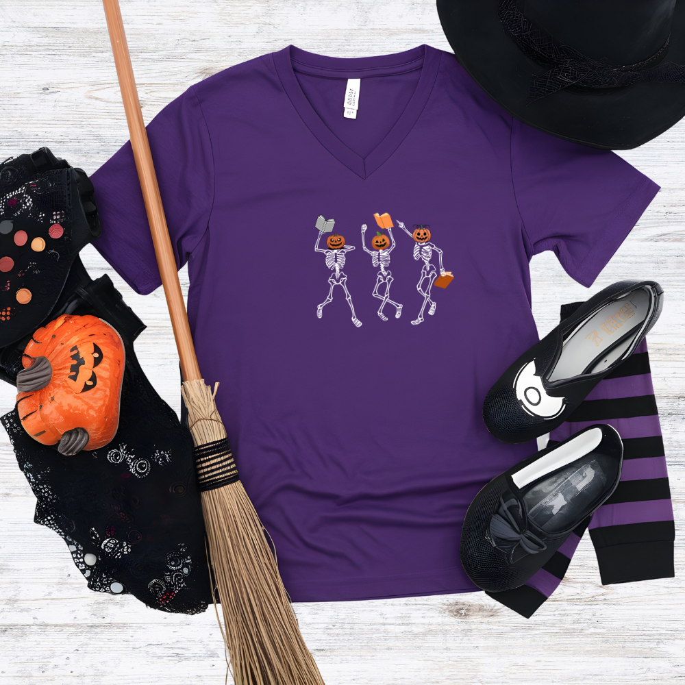 Purple t-shirt with skeleton design, broom, shoes, and hat on a wooden surface
