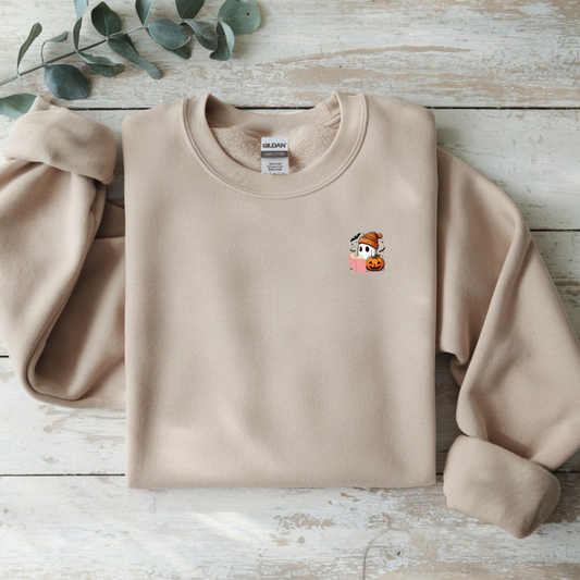 Beige sweatshirt with a small embroidered design on a wooden surface with eucalyptus leaves.