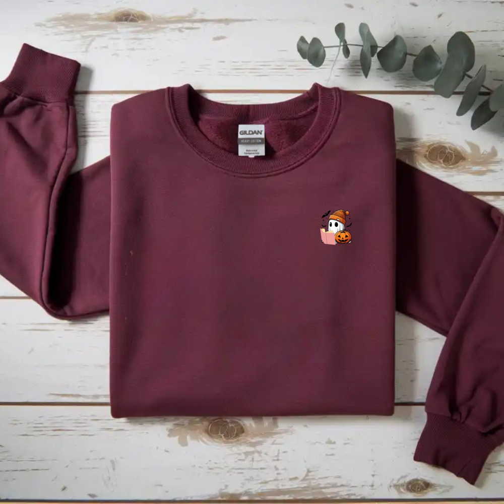 Maroon sweatshirt with a small embroidered design on a wooden surface with eucalyptus leaves.