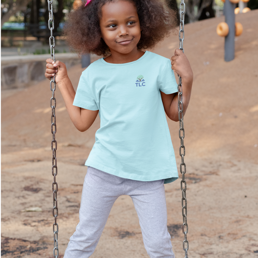 Child on a swing wearing a light blue t-shirt with a logo, standing on a playground.