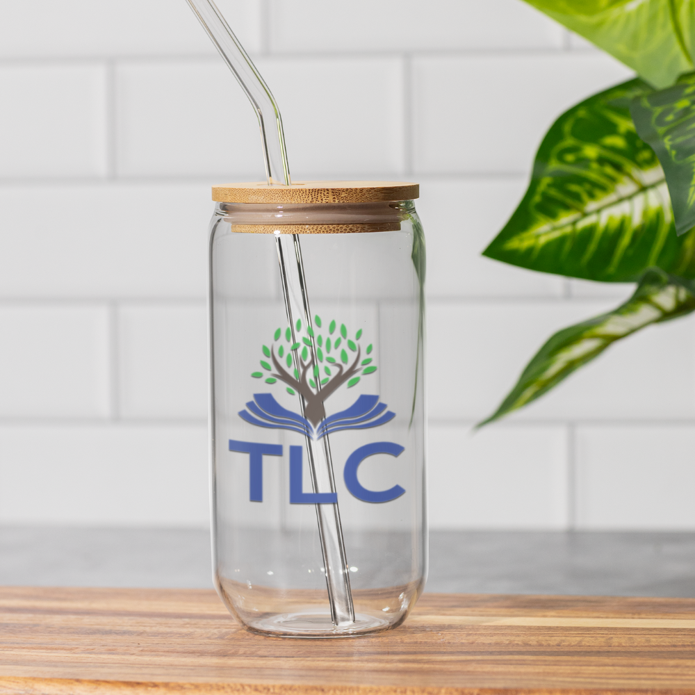 Clear glass tumbler with wooden lid and straw, featuring the TLC logo, on a wooden surface with a plant in the background.