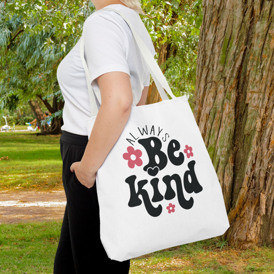 Person holding a tote bag with 'Always Be Kind' text in a park setting