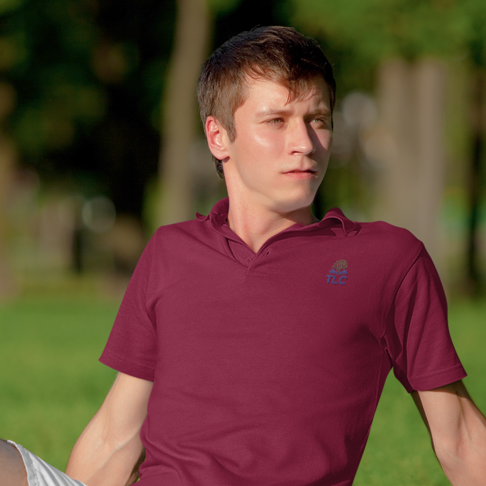 Man wearing a maroon polo shirt with a logo, sitting outdoors on grass.