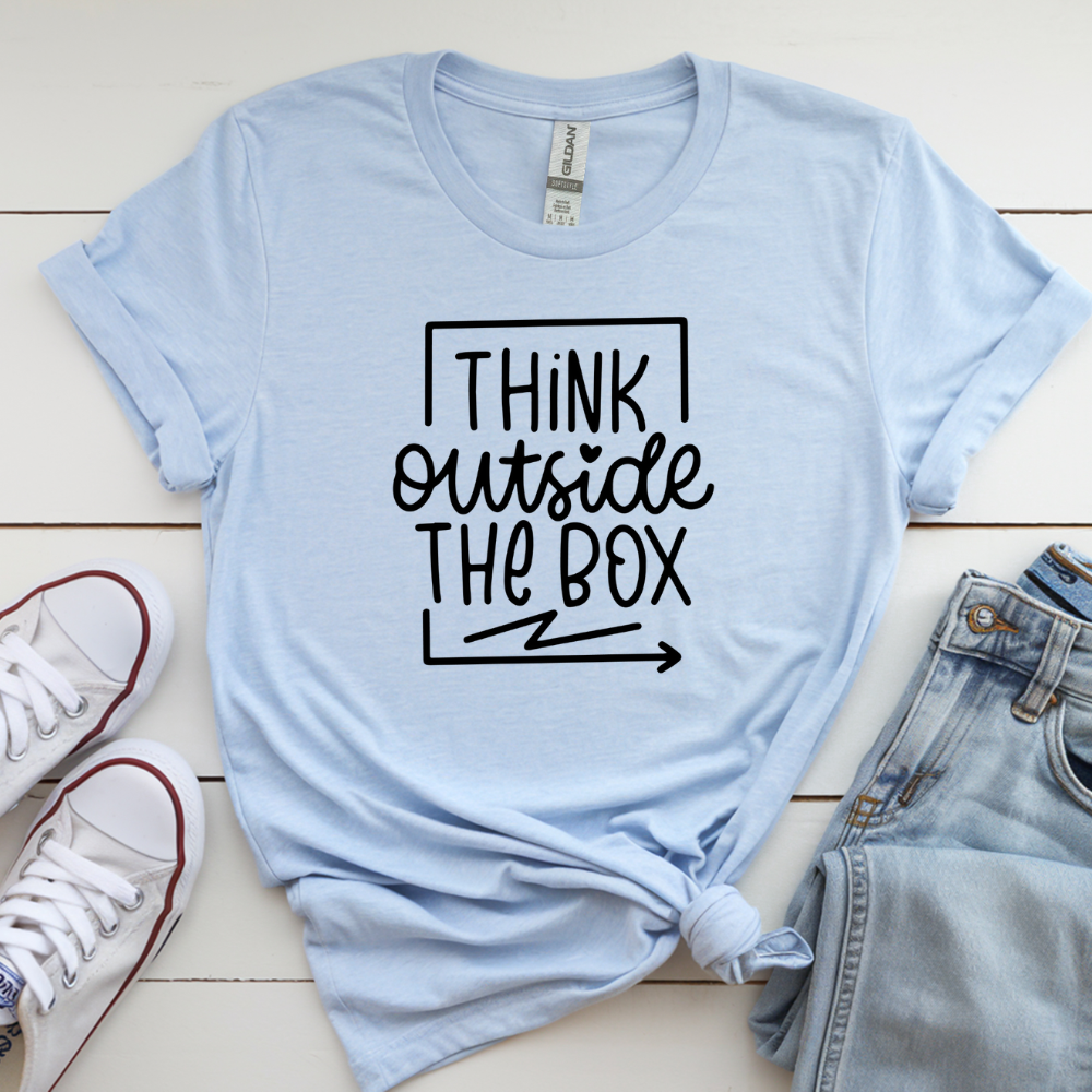 Light blue t-shirt with 'Think Outside The Box' text on a wooden surface with shoes and jeans.