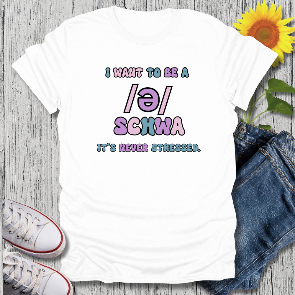 White t-shirt with colorful text, white sneakers, blue jeans, and a sunflower on a wooden surface.