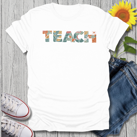 White t-shirt with 'TEACH' printed on it, paired with jeans and sneakers on a wooden surface.