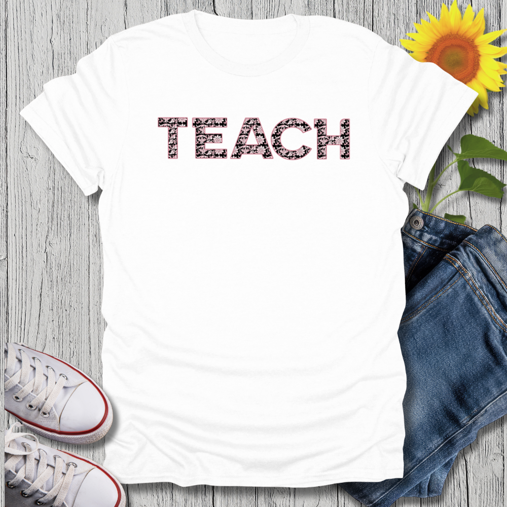 White t-shirt with 'TEACH' printed on it, paired with jeans and sneakers on a wooden surface.