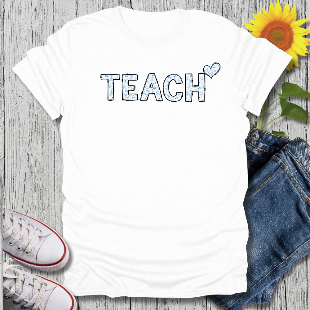 White t-shirt with 'TEACH' text, sunflower, jeans, and sneakers on a wooden surface