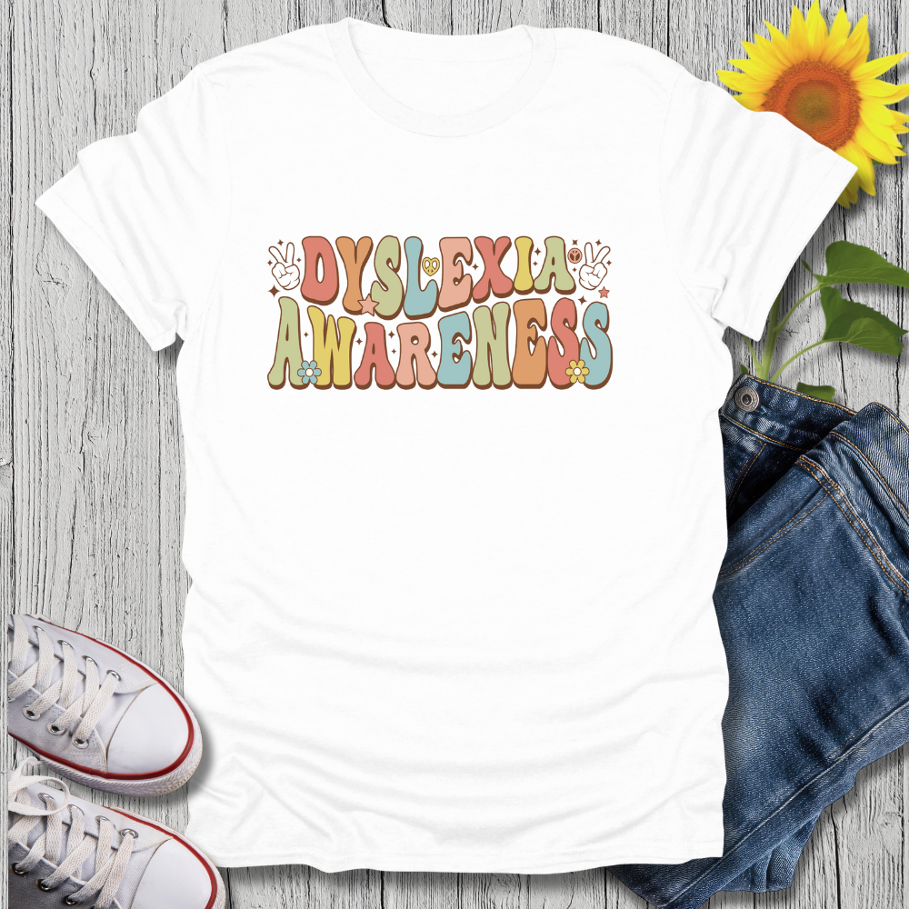 White t-shirt with 'Dyslexia Awareness' text on a wooden surface with jeans and sneakers.