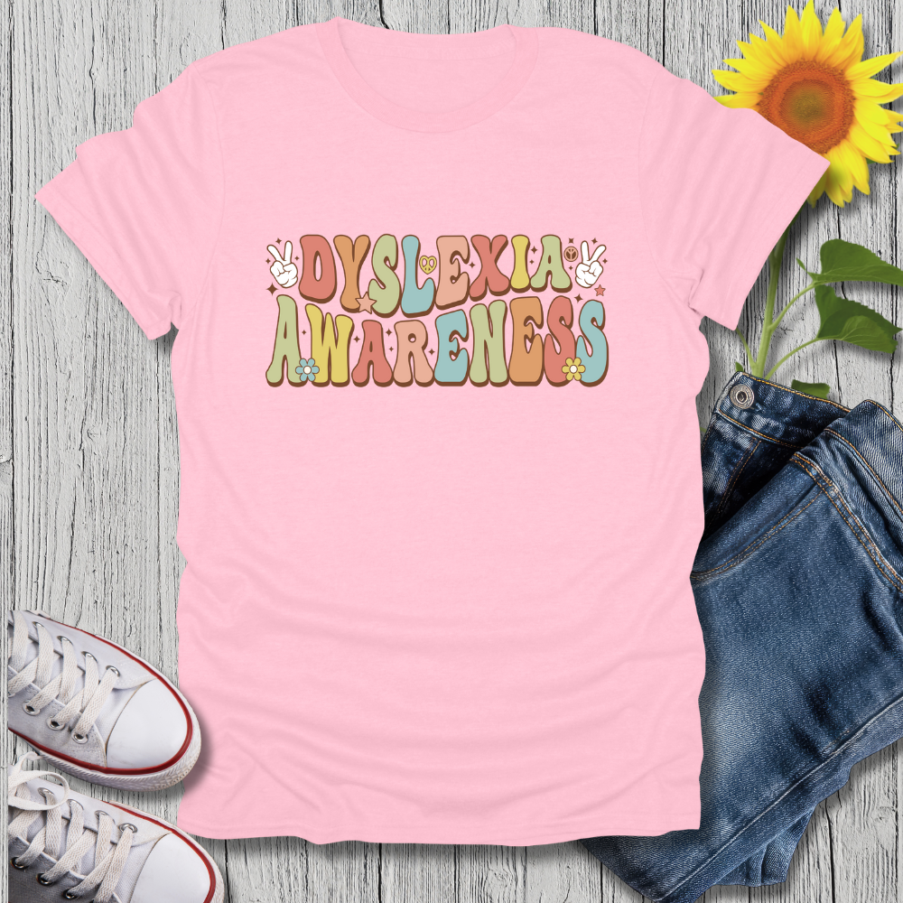 Pink t-shirt with 'Dyslexia Awareness' text on a wooden surface with jeans, sneakers, and a sunflower.