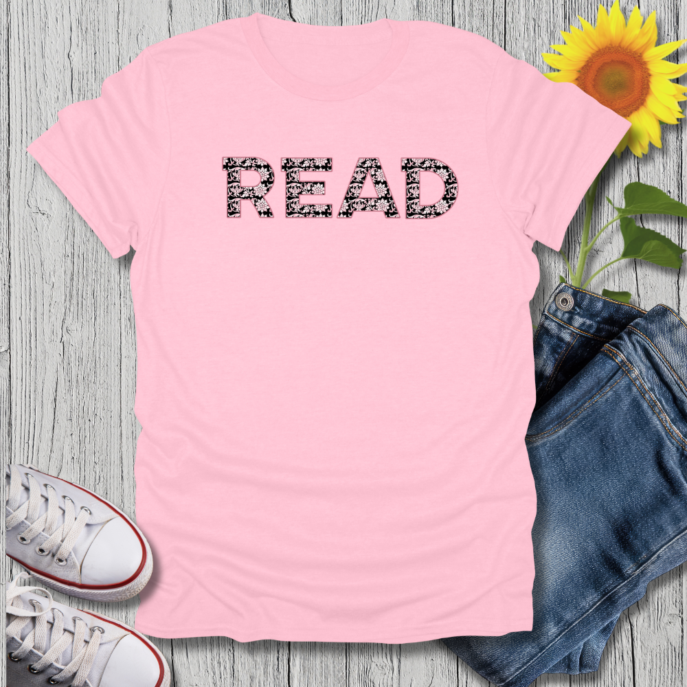Pink t-shirt with 'READ' text, sunflower, jeans, and sneakers on a wooden surface
