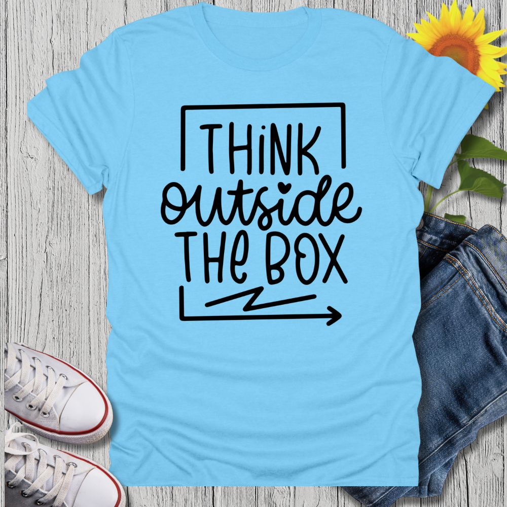 Light blue t-shirt with 'Think outside the box' text on a wooden surface with jeans and sneakers.