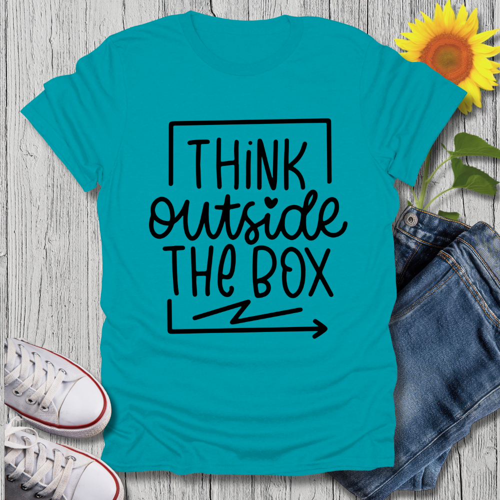 Turquoise t-shirt with 'Think Outside The Box' text on a wooden surface with jeans and sneakers.